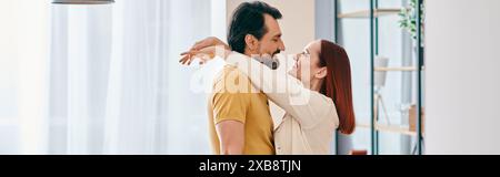 Eine rothaarige Frau und ein bärtiger Mann teilen sich eine warme Umarmung in einem gemütlichen Wohnzimmer und schaffen einen schönen Moment der Intimität und Verbindung. Stockfoto