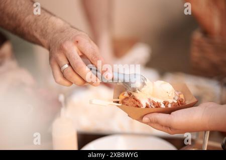 Eine Nahaufnahme einer Hand, die Eis in eine Papierschale schaufelt Stockfoto