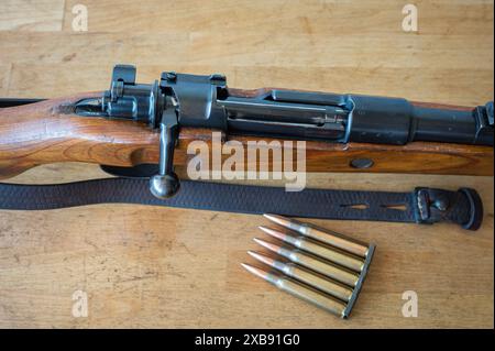 Detail einer Munitionsklammer mit 5 30-06 Kalibern Geschossen neben einem Mauser-Militärgewehr mit Bolzenmechanismus auf einem Holztisch Stockfoto