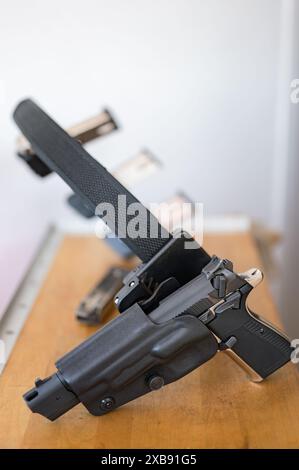 Detail der 9-mm-Pistole, die im Polizeiholster am IPSC-Gürtel eingehängt ist. Oben auf einem Holztisch Stockfoto