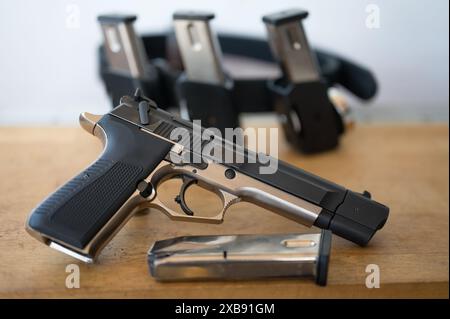 Detail der 9-mm-Pistole mit einem Magazin vor dem IPSC-Band mit den Magazinen. Auf einem Holztisch Stockfoto