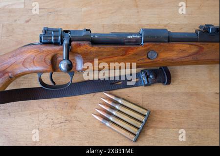 Detail einer Munitionsklammer mit 5 30-06 Kalibern Geschossen neben einem Mauser-Militärgewehr mit Bolzenmechanismus auf einem Holztisch Stockfoto