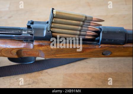 Detail des Einsatzes einer Munitionsklammer mit 5 30-06 Kaliber-Geschossen in ein Mauser-Militärgewehr mit Bolzenmechanismus auf einem Holztisch Stockfoto