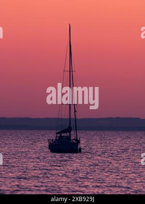 Das Bild zeigt ein ruhiges Segelboot auf dem Wasser bei Sonnenuntergang. Stockfoto