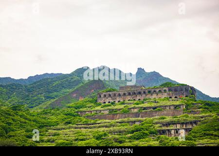 Alte Gebäude auf einem grünen Hügel, umgeben von Büschen und höheren Bergen Stockfoto