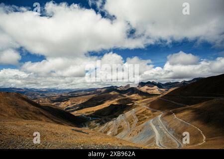 Ein atemberaubendes Bild mit gewundenen Bergstraßen unter einem leuchtend blauen Himmel mit dramatischen Wolken, das die raue Schönheit der Landschaft zeigt. Stockfoto