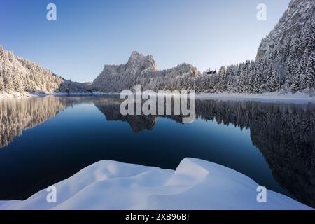 Wunderschöne Winterlandschaft mit Blick auf eine schneebedeckte Bergkette, die sich in einem See mit einer Schneedüne im Vordergrund spiegelt Stockfoto