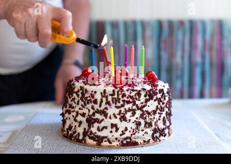 Schwarzwaldkuchen mit Kirschen, Schokoladenchips und Schlagsahne. Geburtstagskuchen. Mann zündet Kerzen an. Shvartsvald Kirschkuchen. Stockfoto