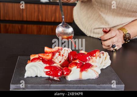 Ein Hauskoch bereitet Meringue zu, legt Erdbeeren auf im Ofen gebackene Meringue. Stockfoto