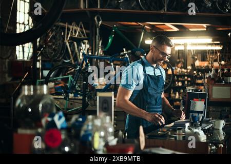 Glücklicher Mann, Fahrradmechaniker und Werkbank mit Werkzeugen in kleinen Unternehmen zur Reparatur, Reparatur oder Wartung. Junge männliche Person, Fahrradingenieur oder Fahrrad Stockfoto