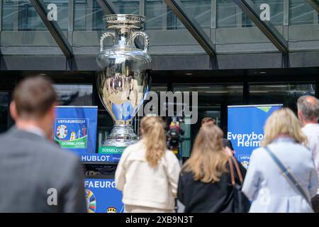 Düsseldorf, Deutschland. Juni 2024. Die Menschen stehen bei der Verleihung der Riesentrophäe vor dem landtag Nordrhein-Westfalen vor dem drei Meter hohen Nachbau der Europameisterschaft. Die Trophäenreplik wird bis zum 13. Juni auf dem Vorplatz des landtags stehen und kann als Selfie-Spot genutzt werden. Quelle: Henning Kaiser/dpa/Alamy Live News Stockfoto