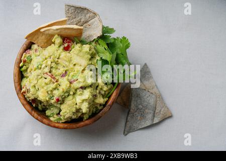 Eine Schüssel mit frisch zubereiteter Guacamole, garniert mit Koriander und serviert mit Chips auf hellem Hintergrund. Die Guacamole ist klobig mit sichtbaren Stücken von t Stockfoto