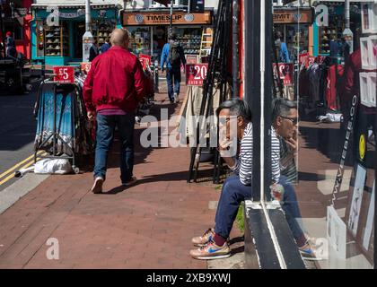 Ein Ladenbesitzer sitzt in der Tür und raucht eine Zigarette in The Lanes, einem zitternden Einkaufsviertel in Brighton, East Sussex, Großbritannien. Stockfoto