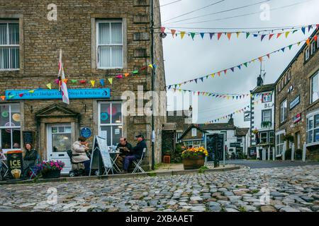 Leute sitzen vor dem Stripey Badger Coffee Shop in Grassington, das eine Kopfsteinpflasterstraße überblickt, North Yorkshire, England, Großbritannien Stockfoto