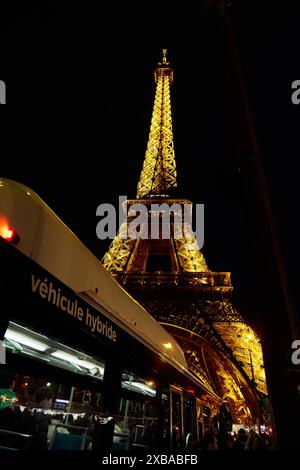 Ein hybrider öffentlicher Bus fährt bei Nacht an der Eiffeltour in Paris vorbei Stockfoto