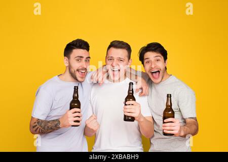 Drei Freunde jubeln mit Bier auf Gelb Stockfoto