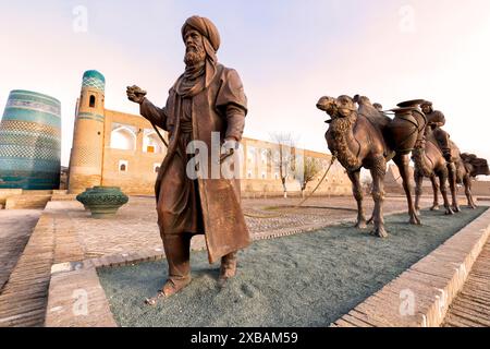 Chiwa, Usbekistan - 29. März 2024: Skulpturengruppe einer antiken Karawane mit Kamelen, die verschiedene Güter entlang der Seidenstraße transportieren, und zwei Männer in Tradi Stockfoto