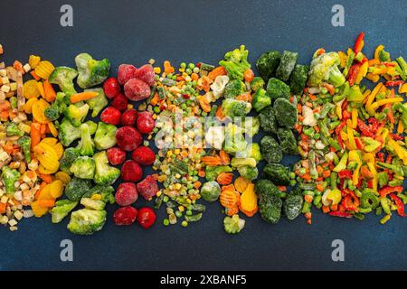 Zubereitung von frischem Gemüse im Sommer für den Winter, verschiedene gefrorene Gemüse und Beeren auf dunkelblauem Hintergrund, Draufsicht Stockfoto