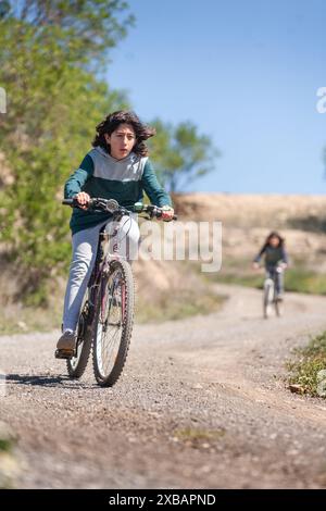 Teenager auf dem Fahrrad, der einen kurvenreichen Weg hinunterfährt. Im Hintergrund wird er von einem anderen Jungen begleitet. Outdoor-Aktivitäten. Stockfoto