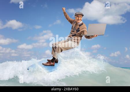 Ein älterer Mann, der auf einer Welle im Meer auf einem Surfbrett reitet und einen Laptop hält Stockfoto