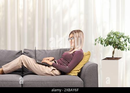 Junge Frau, die an einem Laptop arbeitet und zu Hause auf einem Sofa liegt Stockfoto