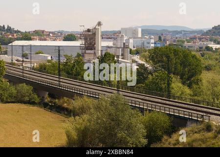 Barcelona, Spanien - 15. Mai 2023: Eine Eisenbahnlinie führt durch eine Szene, die von Industriefabriken und Lagerhäusern dominiert wird, unter klarem Himmel. Stockfoto