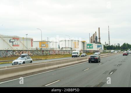 Lyon, Frankreich - 16. Mai 2023: Neben einer befahrenen Autobahn ist eine Industrieanlage mit Lagertanks mit Graffiti zu sehen, im Hintergrund Smok Stockfoto