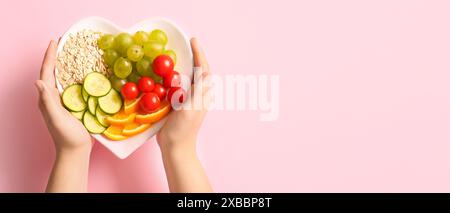 Hände halten herzförmige Platte mit gesunden Produkten auf rosa Hintergrund mit Platz für Text Stockfoto