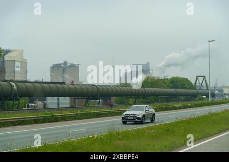 Gent, Belgien - 22. Mai 2023: Ein Auto fährt eine Straße neben einer großen Fabrik entlang. Das industrielle Umfeld steht im Gegensatz zum Fahrzeug, dem Showcasin Stockfoto