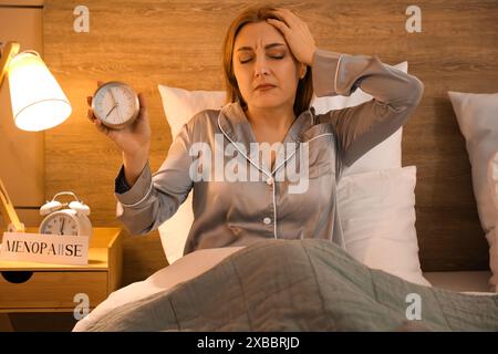 Reife Frau mit Wecker kann nachts nicht im Schlafzimmer schlafen. Menopause-Konzept Stockfoto