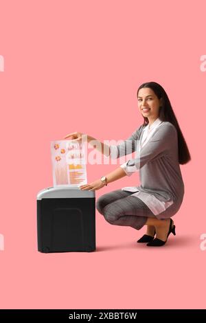 Junge Frau, die Dokumente mit Aktenvernichter auf rosa Hintergrund zerstört Stockfoto