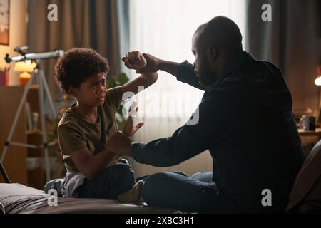 Seitenansicht Porträt von Vater und Sohn, die aggressiv auf dem Bett sitzen, in dramatischem Licht Kopierraum Stockfoto