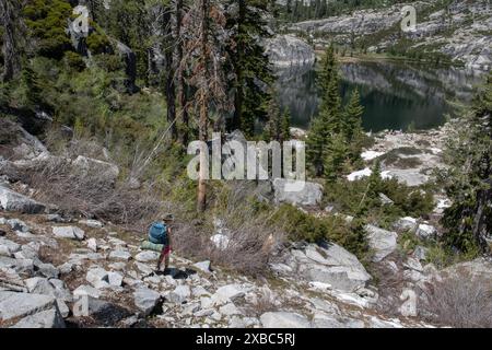 Wanderer oder Rucksacktouristen, die einen felsigen Berghang hinunter in Richtung eines hohen Sees in der Ferne in der Wildnis der Trinity Alps in Kalifornien hinunterfahren. Stockfoto