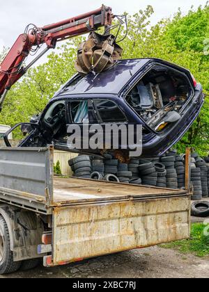 Das Verladen eines verlassenen Wracks mit einem hydraulischen Lader, der auf einem Abschleppwagen montiert ist, das Fahrzeug wird zur Entsorgung gebracht und auf die Recyclingstelle gebracht Stockfoto