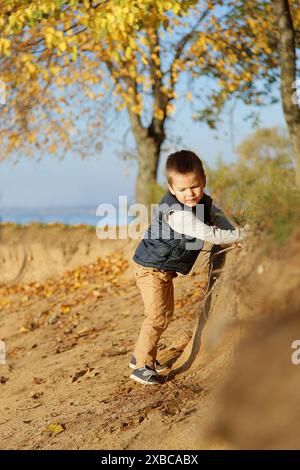 Ein kleiner Junge, der auf einem Sandweg in einer Herbstlandschaft mit gelben Blättern und Bäumen im Hintergrund spielt, Weißrussland. Minsk Stockfoto