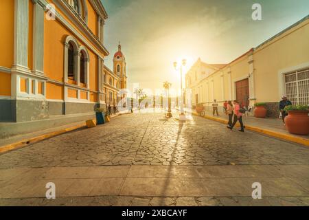 Stadtblick auf die Menschen, die bei Sonnenuntergang durch die Straßen der Kathedrale von Granada laufen. Granada, Nicaragua. 05.10.2024 Stockfoto