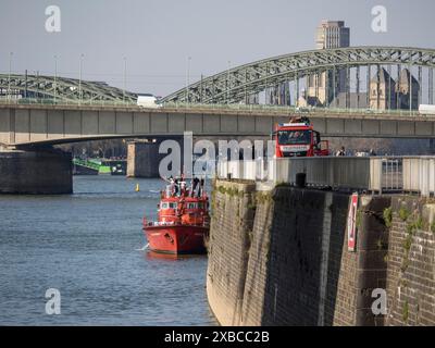 Feuerwehrboot auf dem Fluss in der Nähe einer Brücke mit Stadtblick und architektonischen Sehenswürdigkeiten im Hintergrund, Köln, Nordrhein-Westfalen, Deutschland Stockfoto