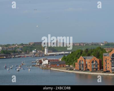 Ein Fluss mit Booten und Häusern, umgeben von grünen Hügeln unter blauem Himmel, newcastle upon thyne, england, Großbritannien Stockfoto