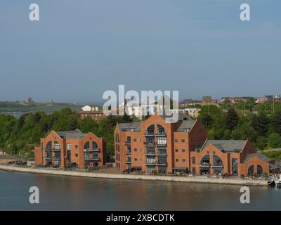 Große Backsteinhäuser am Flussufer, umgeben von Grünflächen unter blauem Himmel, newcastle upon thyne, england, Großbritannien Stockfoto