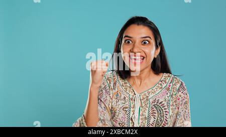 Porträt einer fröhlichen indianerin, die feiert, positive Emotionen zeigt und glücklich ist. Begeisterte Person begeistert von Leistung, Anfeuern und Gestikulieren, Studiohintergrund, Kamera B Stockfoto