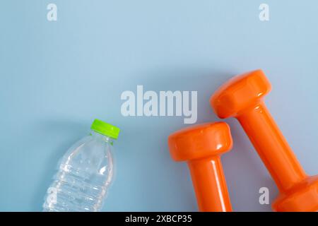 Kreatives Layout aus orangen Kurzhanteln und einer Flasche Wasser auf hellblauem Hintergrund. Minimale Fitness, gesunder Lebensstil und Sportkonzept. Stockfoto