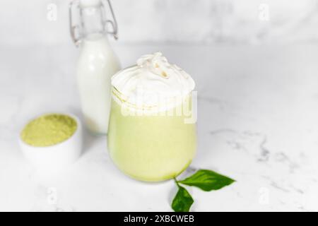 Matcha grüner Tee in einem Glas mit Schlagsahne auf hellgrauem Hintergrund. Grüner Tee. Stockfoto