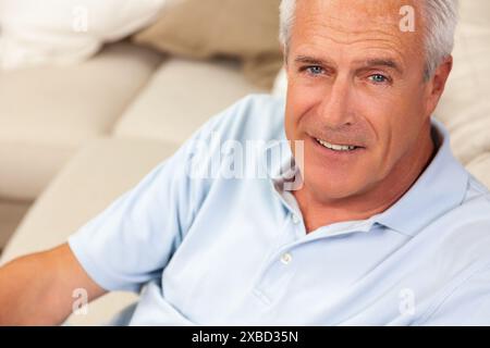 Glücklicher und gesunder älterer oder mittlerer Alter Mann sitzt auf einem Sofa zu Hause lächelnd und glücklich Stockfoto