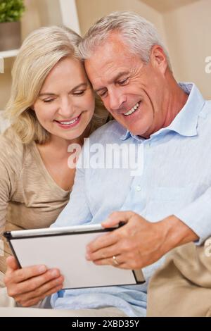 Glücklich senior Mann und Frau Paar zusammen zu Hause sitzen lächelnd und glücklich unter Verwendung eines Tablet-Computers Stockfoto