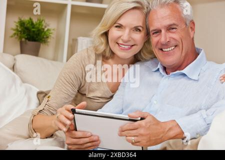 Glücklich senior Mann und Frau Paar zusammen zu Hause sitzen lächelnd und glücklich unter Verwendung eines Tablet-Computers Stockfoto