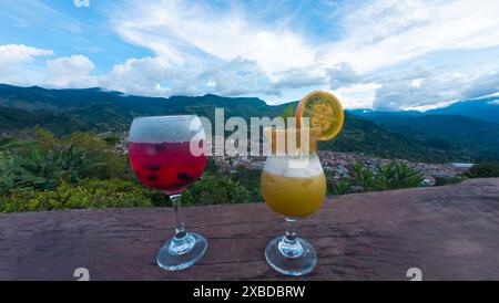 Zwei bunte Fruchtcocktails auf einem Holztisch mit atemberaubendem Berglandschafthintergrund. Stockfoto