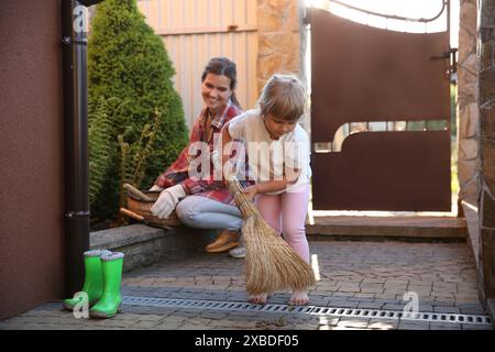 Mutter und ihre süße Tochter putzen zusammen in der Nähe des Hauses am Frühlingstag Stockfoto