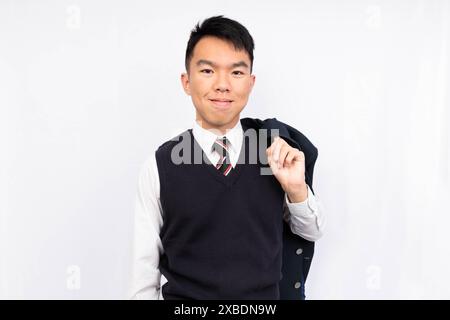 Ein gut gekleideter Jugendschüler in Weste und Krawatte zieht seinen Blazer lässig über die Schulter. Er trägt seine Schuluniform. Stockfoto