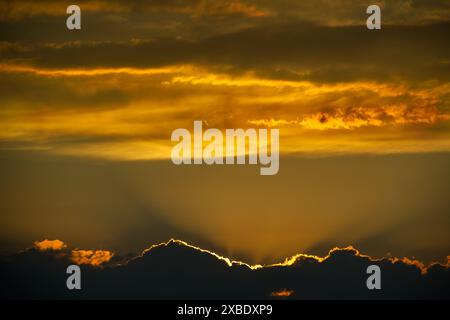 Atemberaubender goldener Sonnenuntergang mit Sonnenstrahlen, die durch dunkle Wolken brechen und einen dramatischen Himmel schaffen. Stockfoto