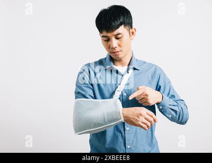 Porträt asiatischer lächelnder junger Mann, der einen Gips auf seinem Arm trägt gebrochenes Atelier, isoliert weiß Stockfoto